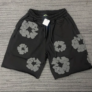 Svarta Denim tears shorts - Svarta Denim Tears shorts med stora gråa blommor tryckta över hela tyget. De har resår i midjan och snörning för justerbar passform. Perfekta för en avslappnad stil och har en normal passform.
