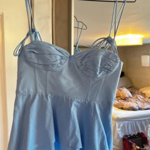 Ljusblå linnetopp från Zara - Supersöt ljusblå linnetopp från Zara med tunna axelband som knyts på axlarna. Toppen har en söt byst med veckade detaljer och lätt utsvängd nederdel. Perfekt för varma dagar och enkel att styla med jeans eller kjol.