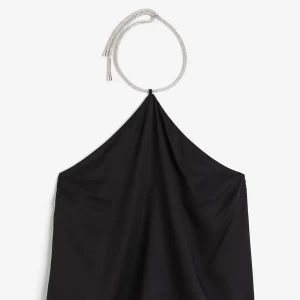 Svart halterneck topp med glittrande band - Snygg svart halterneck topp med glittrande silverfärgat band som knyts runt halsen. Perfekt för att sticka ut med en elegant touch. Toppens material har en mjuk och slät känsla.
