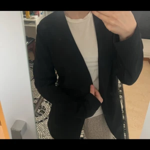 Svart kavaj - Stilren svart kavaj med klassisk passform. Perfekt att slänga över en t-shirt för en snygg och enkel look. Långa ärmar och enkel design utan synliga detaljer.