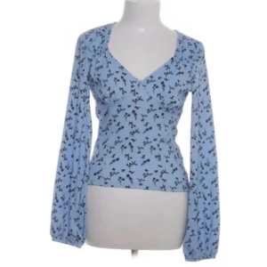 Blå blommig långärmad topp med knyt i ryggen - Supersöt blå långärmad topp med svart blommönster och ribbad struktur. Toppen har v-ringning framtill och snygg öppen rygg med knytband. Perfekt för dig som gillar unika detaljer och trendig stil.