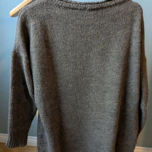 Kaki stickad tröja - Mysig grå stickad tröja med rund halsringning och långa ärmar. Tröjan är enkel och stilren, perfekt att slänga på sig när det är kyligt ute. Materialet består av 70% akryl och 30% ull för en skön känsla.