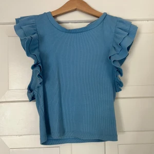 Blå topp med volang från Zara - Säljer en ljusblå ribbad topp från Zara med volangdetaljer längs ärmhålen. Använd ganska mycket och säljer då den är för liten. Storlek S men passar även xs. 
