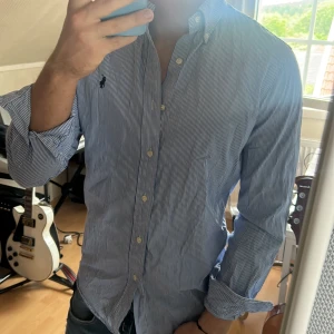 Blåvit randig skjorta från Polo Ralph Lauren - Säljer en klassisk blåvit randig skjorta från Polo Ralph Lauren i storlek S. Skjortan har lång ärm, knappar framtill och en broderad logga på bröstet. Perfekt för en stilren och tidlös look. defekt på sista bild