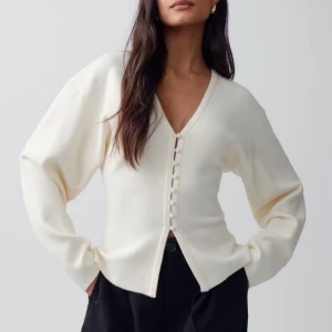 Vit kofta med v-ringning och knappar - Snygg vit kofta med v-ringning och knappar framtill. Tröjan har långa ärmar och en avslappnad passform, perfekt att styla till både jeans och kjol. Enkel och stilren design som passar till många tillfällen.