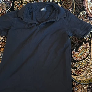 Svart pikétröja från Cutter & Buck - Klassisk svart pikétröja från Cutter & Buck med krage och korta ärmar. Perfekt för en stilren och avslappnad look. Tröjan har en enkel design utan mönster eller extra detaljer.