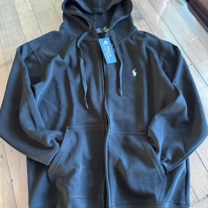 Svart hoodie med dragkedja från Polo Ralph Lauren - Svart hoodie från Polo Ralph Lauren med dragkedja, helt NY och priest kan diskuteras.