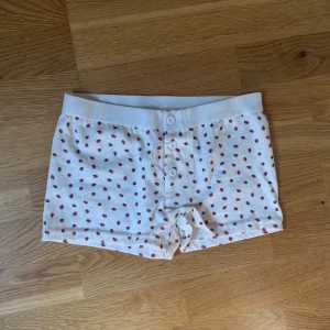 Vita bomullsshorts med röda jordgubbar - Söta vita shorts med röda jordgubbar och knappar framtill. Mjukt och stretchigt material med bred resår i midjan. Perfekta för en avslappnad stil. Coquette brandy Melville shorts med jordgubbar på  Den är ny men prislappen är av men snöret är fortfarande på  Söt men jordgubbar på, perfekt till pyjamas eller sommaren   Passar XS och S