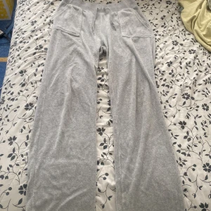 Grå Juicy byxor med fickor och snörning - Säljer ett par grå mjukisbyxor med bred resår i midjan och snörning framtill. Byxorna har stora fickor fram och bak, bakfickorna har knappar. Modellen är rak och lös, perfekt för en avslappnad stil.