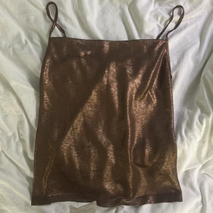 Bronsfärgad glittrig klänning från Zara - Säljer en snygg bronsfärgad glittrig topp från Zara med smala axelband och rak passform. Klänningen har en kort längd och skimrande material som ger en cool look. Perfekt för dig som vill sticka ut!