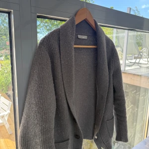 Grå stickad kofta från Guido Maria Kretschmer - Mysig grå stickad kofta med bred krage och knappar framtill. Koftan har två fickor och ett ribbat mönster som ger en stilren look. Den är i storlek L men har krymp i tvätten till storlek S kanske till och med lite mindre. 