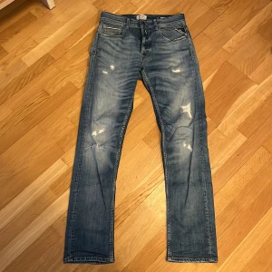 Replay jeans modell Grover  - Säljer ett par blå jeansbyxor med raka ben och slitna detaljer framtill. Klassisk femficksmodell med dragkedja och knapp. Jeansen har en normal passform och är perfekta för en avslappnad stil. 