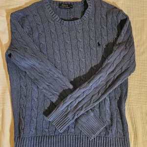 Blå kabelstickad tröja från Polo Ralph Lauren - Säljer en klassisk blå kabelstickad tröja från Polo Ralph Lauren. Tröjan har rund halsringning, långa ärmar och ribbade muddar. Perfekt för lager-på-lager och snygg till både jeans och kjol. Ikonisk liten logga broderad på bröstet. Storlek S 