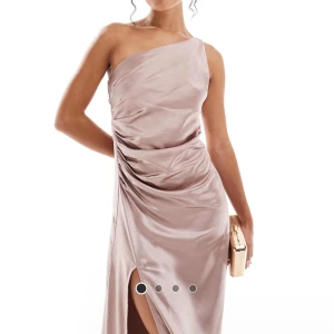 Champagne/rosafärgad långklänning med slits och oneshoulder - Elegant långklänning i champagnefärgad satin med oneshoulder-design och hög slits. Klänningen har draperade detaljer längs sidan för en snygg siluett. Perfekt för speciella tillfällen. Helt ny, aldrig använt men säljer för att Retur tiden gick ut och jag hittade en annan klänning jag skulle använda till balen. Storlek 38. Kostar 1 250kr nypris och är helt slutsåld på hemsidan, (ASOS)