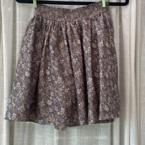 Blommig kortkjol med resårmidja - Säljer en söt kortkjol med småblommigt mönster i lila, beige och bruna toner. Kjolen har en bred resår i midjan och är fodrad . Perfekt för våren. 