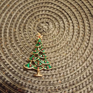 Julgransbrosch i guld och grönt - Säljer en brosch i form av en julgran med gröna och röda detaljer samt guldfärgad ram. Perfekt accessoar för att sprida julkänsla! Fästes enkelt på kläder eller väska.