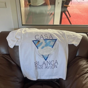 Vit t-shirt med svanmotiv från Casablanca - Vit t-shirt från Casablanca med stort tryck av en svan och texten 'Casa Blanca Par Avion' på framsidan. Klassisk passform och rund halsringning. Perfekt för dig som gillar unika prints och stilrena plagg.