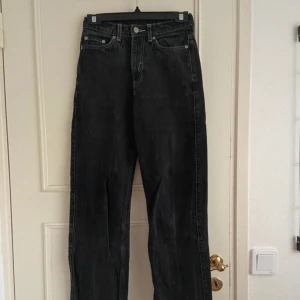 Svarta jeans hög midja - Klassiska svarta jeans med hög midja och raka ben. Jeansen har fem fickor, knappgylf och är tillverkade i robust denim. Perfekta för en avslappnad och tidlös stil.