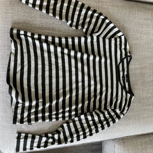 Randig långärmad tröja Tiger of Sweden - Snygg långärmad tröja från Tiger of Sweden Jeans i svart och grått med klassiskt randigt mönster. Tröjan har rund halsringning och är tillverkad i mjukt material som känns skönt mot huden. Perfekt för dig som gillar stilren och enkel design.