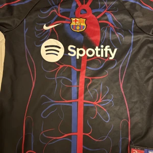 FC Barcelona Nike fotbollströja Spotify - Unik FC Barcelona fotbollströja från Nike med Spotify-logga på bröstet. Svart bas med blå och röda detaljer som liknar blodkärl och hjärta, samt klubbmärke på bröstet. Kortärmad och tillverkad i lätt, andningsbart material.