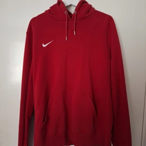 Röd Nike hoodie - Röd hoodie från Nike i storlek L med klassisk vit swoosh-logga på bröstet. Hoodien har huva med snörning, stor magficka och långa ärmar. Perfekt för chill dagar eller när du vill ha en sportig look.