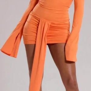 Orange/korall offshoulder kort klänning - Trendig orange kortklänning med offshoulder-design och långa utsvängda ärmar. Klänningen har en snygg drapering och knyt-detalj framtill som ger en cool och unik look. Perfekt för dig som vill sticka ut med färg och form.