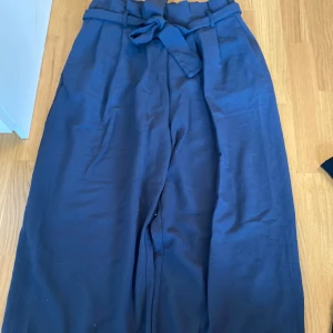Mörkblå vida byxor med knytband i strl M - Snygga mörkblå byxor med hög midja och brett knytband i midjan. Byxorna har en loose och wide passform med raka, vida ben. Perfekta för en chill och stilren look. I strl M