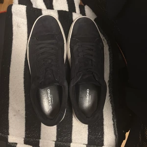Svarta sneakers från Vagabond - Stilrena svarta sneakers från Vagabond med ovandel i mocka och klassisk vit sula. Skorna har rund tå, platt sula och snörning framtill. Perfekta för en clean och avslappnad look.