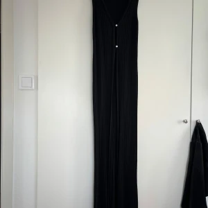 Svart ribbad lång väst Lindex S - Svart ribbad lång väst från Lindex i storlek S. Västen  är ärmlös med djup v-ringning och två knappar framtill. Den har en tight passform och är tillverkad i ett stretchigt material som sitter snyggt på kroppen.