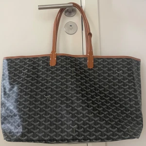 Svart väska med mönster - Säljer en svart shoppingväska med grafiskt mönster och bruna detaljer. Väskan har rymligt innerfack och medföljande liten väska i samma design. 