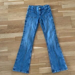 Blå bootcut jeans från Gina Tricot - Snygga blå jeans från Gina Tricot i storlek 158. Modellen har bootcut-ben, hög midja och markerade sömmar framtill. Jeansen har två stora fickor fram och två bak, samt bälteshällor. Perfekta för en trendig och avslappnad look.