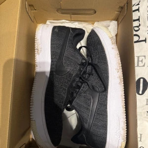 Svarta Nike Air Force 1 sneakers - Snygga svarta Nike Air Force 1 sneakers med stickad ovandel och klassisk vit sula. Skorna har svarta skinnswooshes på sidorna och svart snörning. Perfekta för dig som gillar en stilren och sportig look.
