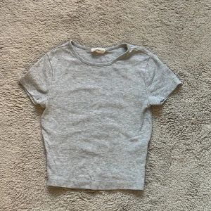 Grå croppad t-shirt från Gina tricot - En enkel och stilren grå croppad t-shirt från Gina tricot. T-shirten har rund halsringning och korta ärmar, perfekt för en avslappnad look. Tillverkad i mjuk bomull som känns skön mot huden.