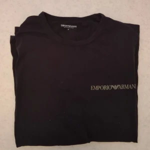 Svart t-shirt Emporio Armani PRIS KAN DISKUTERAS  - Svart t-shirt från Emporio Armani med klassisk rund hals och diskret logga tryckt på bröstet. T-shirten är i mjuk bomull och har en enkel, stilren design som passar perfekt till jeans eller shorts.