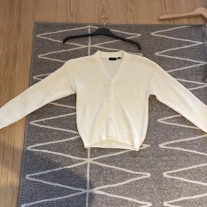 Vit ribbstickad kofta från XOXO Friends - Superfin vit kofta från XOXO Friends i ribbstickat material. Koftan har v-ringning, stora knappar framtill och långa ärmar. Perfekt att slänga över en t-shirt för en chill look. Passar dig som gillar enkel och stilren vibe.