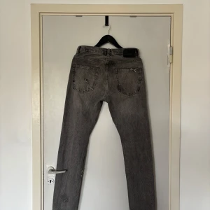 Grå slitna jeans  - Säljer ett par grå jeans med slitningar och trasiga detaljer på både fram- och baksida. Klassisk femficksmodell med raka ben och normal passform. Jeansen har en snygg vintagekänsla och är tillverkade i bomull.