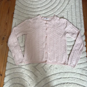 Kabelstickad, Ljusrosa kofta från Uniqlo - Supersöt ljusrosa kofta från Uniqlo med klassiskt kabelstickat mönster. Rund halsringning, knappar framtill och långa ärmar. Perfekt för lager-på-lager och ger en mjuk, chill vibe till din outfit. Har dock ett litet hål på ryggen men går lätt att sy igen. Det är tecken på tvättning och därför kommer jag sälja för lite billigare pris.