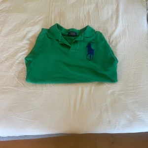 Grön pikétröja Polo Ralph Lauren storlek 10-12 år - Snygg grön pikétröja från Polo Ralph Lauren i storlek M. Tröjan har klassisk krage, korta ärmar och stor blå logga på bröstet samt en blå siffra 3 på ena ärmen. Tillverkad i bomull, perfekt för en sportig och stilren look.