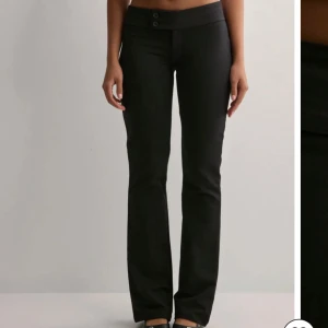Svarta bootcut byxor med låg midja - Snygga svarta byxor med bootcut-snitt och låg midja. Byxorna har två knappar framtill och är perfekta för en trendig och stilren look. Passar dig som gillar klassiska svarta byxor med en modern twist.