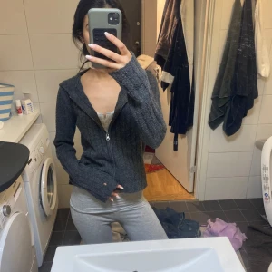 Mörkgrå stickad cardigan jacka - Mysig mörkgrå stickad cardigan jacka med dragkedja framtill. Jackan har ribbad struktur, lång ärm och en lite loose passform. Perfekt att slänga på sig när det är kyligt ute.