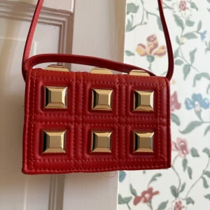 Röd/orange axelväska med guldiga nitar - Röd/orange axelväska från Zara. Väskan är i fint skick förutom slitage i ena kanten, se bild. Därav det låga priset. 