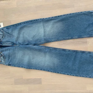 Blå wide jeans från H&M, stl 38 - Säljer ett par ljusblå jeans från H&M i storlek 38. Modellen har hög midja och raka, vida ben för en avslappnad look. Jeansen är tillverkade i denim med 20% återvunnen bomull och har klassiska femficksdetaljer.