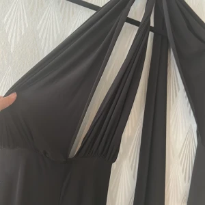 Svart jumpsuit ( knyt hur du vill )  - Supersnygg svart jumpsuit med djup v-ringning och långa omlottband som kan knytas på olika sätt. Klänningen har en elegant och slimmad siluett, perfekt för att sticka ut. Materialet är mjukt och följsamt, vilket ger en lyxig känsla. Från Rebecca Stella ! 