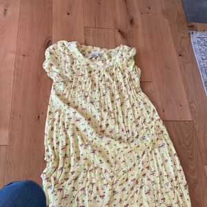 Gul blommig klänning från Isolde - Söt gul klänning från Isolde med små blommor i rosa och svart. Klänningen har korta ärmar, lös passform och är perfekt för varma dagar. Lätt och luftig, med romantisk känsla och rynkade detaljer vid halsen.