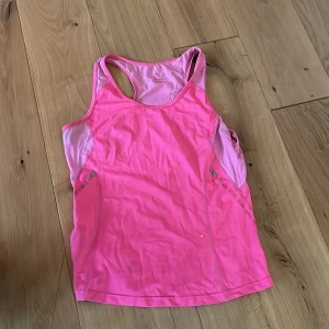 Rosa linnetopp från North Bend - Sportig rosa linnetopp från North Bend med brottarrygg och meshpaneler på sidorna för extra ventilation. Perfekt för träning eller löpning, tillverkad i lätt och snabbtorkande syntetmaterial. Snygg passform och bekväm att ha på sig under aktiva dagar.