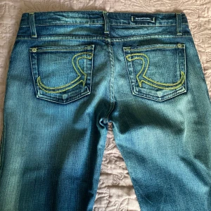 Rock & Republic Jeans  - Vintage lågmidjade och utsvängda jeans med snygga bakfickor. Liten defekt som visas i bild 4. Byxorna är den 2003, strl 29, Midjemått:40cm, Längd:110cm Innerben:84cm.