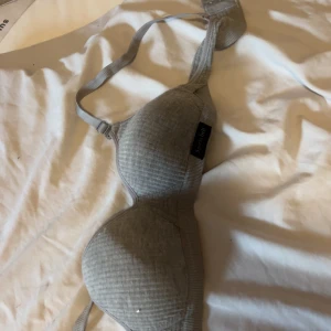 Grå ribbad bh-topp från Spirit Label - Grå bh-topp från Spirit Label med ribbad struktur och justerbara axelband. Toppen har mjuka kupor och klassisk hysk- och hakknäppning bak. Perfekt för dig som gillar en enkel och stilren look med bekväm passform.