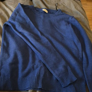 Blå stickad tröja från Vila - Mysig blå stickad tröja från Vila med rund halsringning och ribbade muddar vid ärmslut och nederkant. Perfekt för lager-på-lager och enkel att matcha med jeans eller kjol. Klassisk modell med lång ärm och relaxed fit.