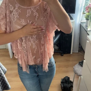 Rosa spetsblus - Superfin ljusrosa blus i spets från Lindex med volangiga korta ärmar och blommigt mönster. Blusen är transparent och har en lös passform, perfekt att styla över ett rosa linne eller en BH. Tveka inte att fråga om du undrar något! 💌