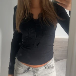 Svart långärmad topp med spets - Snygg svart långärmad topp med v-ringning och spetsdetaljer framtill. Tight passform som framhäver figuren och passar perfekt till jeans eller kjol. Enkel men ändå med en extra touch tack vare spetsen.